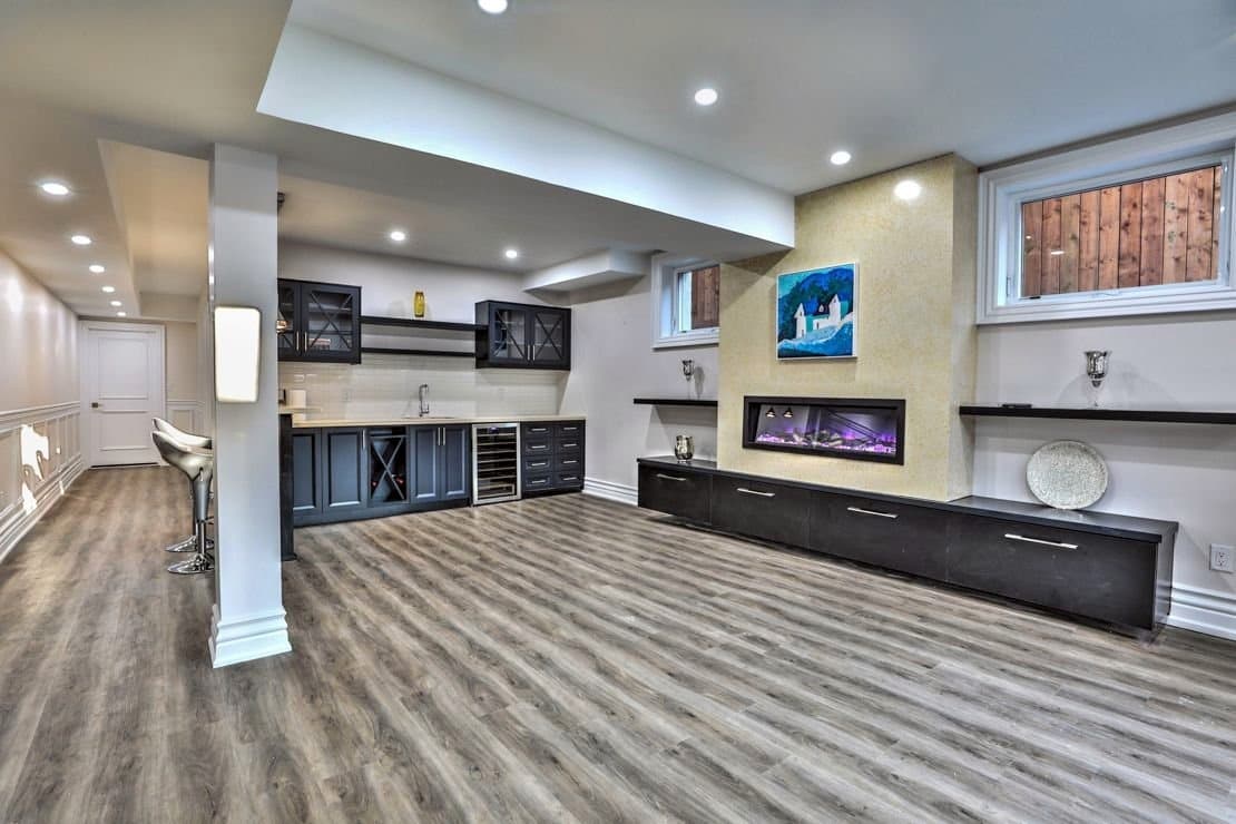 Basement wet bar in navy cabinetry with a linear fireplace and floating shelves