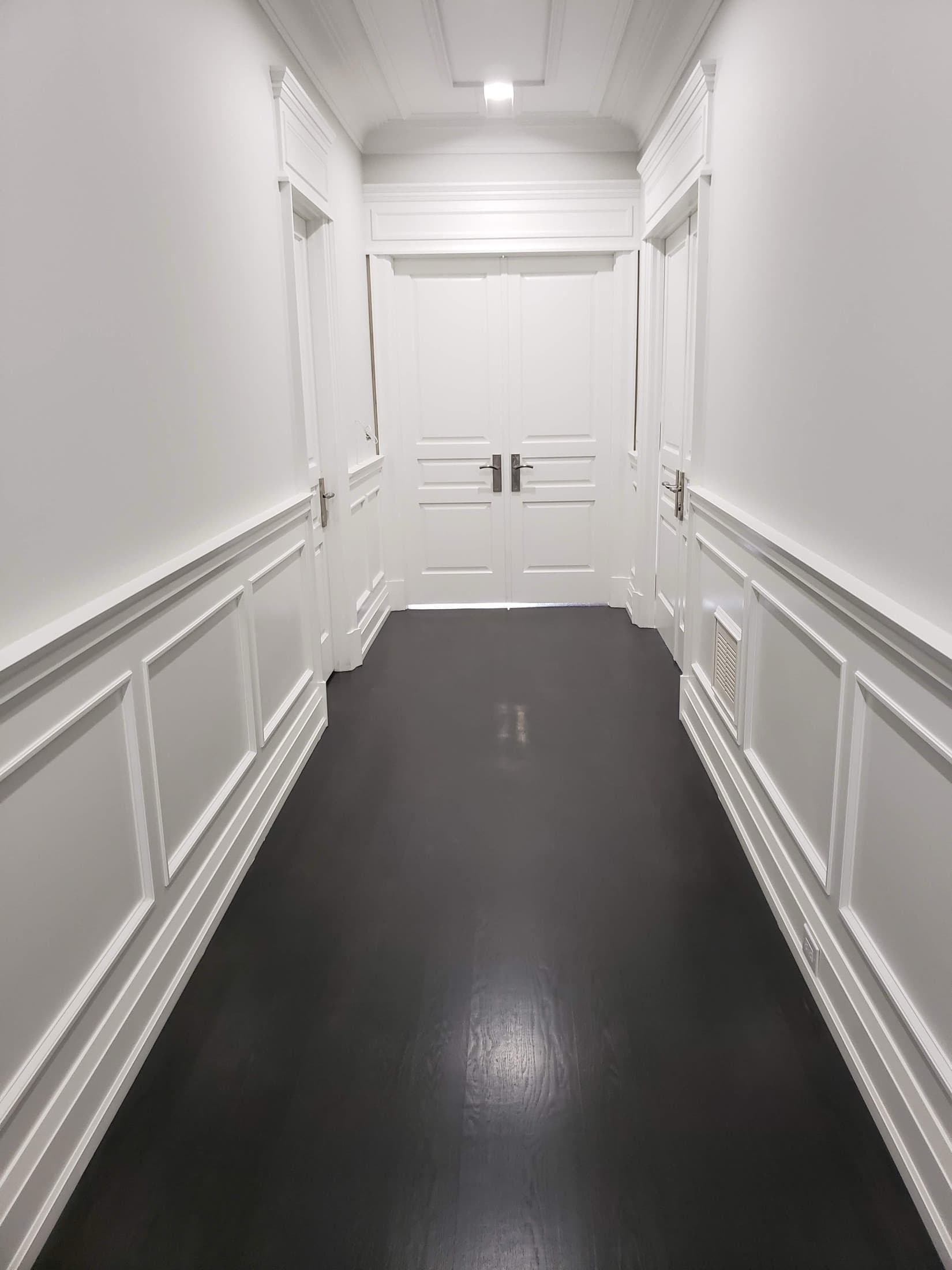 White panelled double doors at the end of a wainscoted hallway