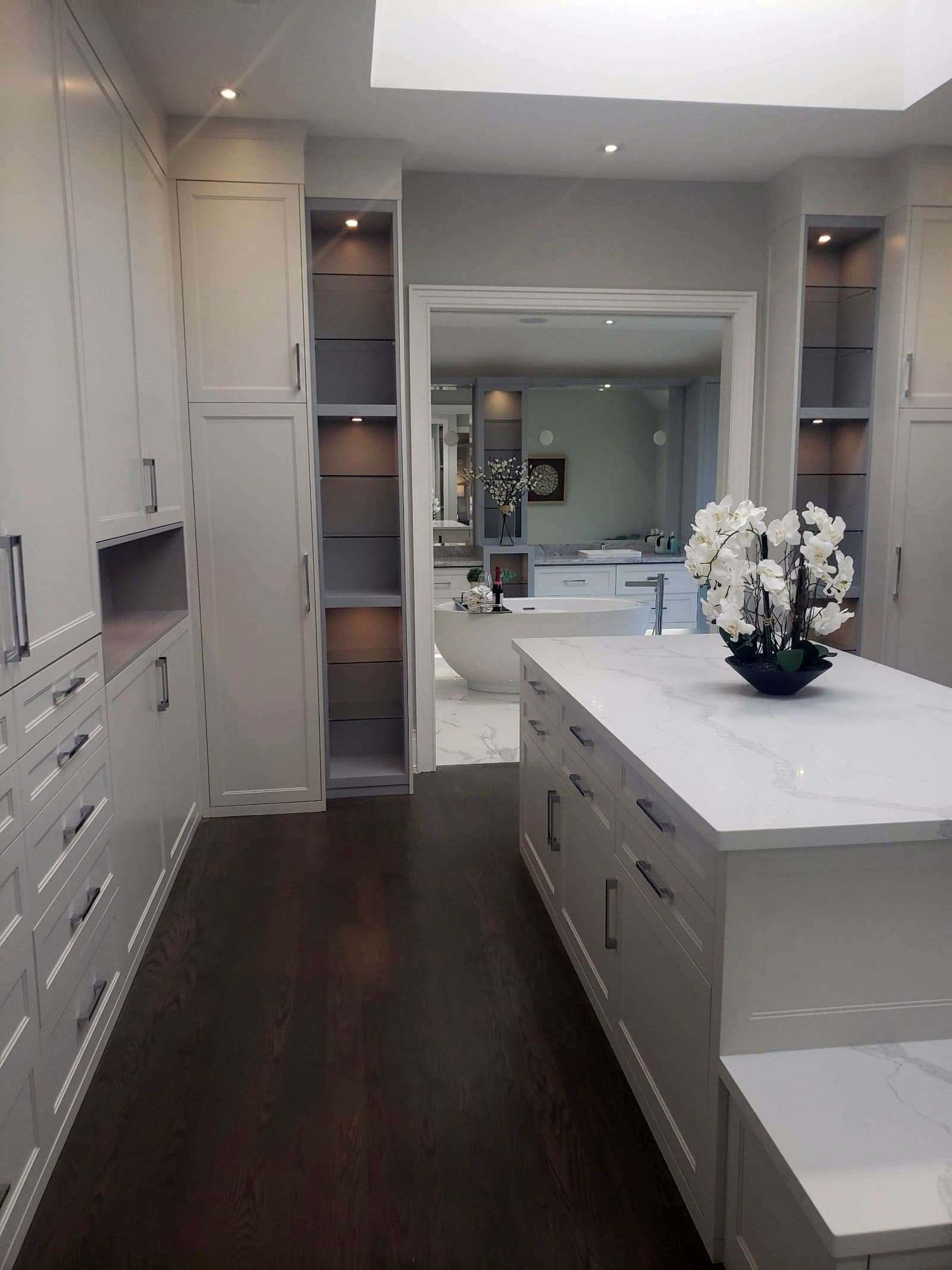 Dressing room with a stone topped island and lit shelving, opening to an ensuite