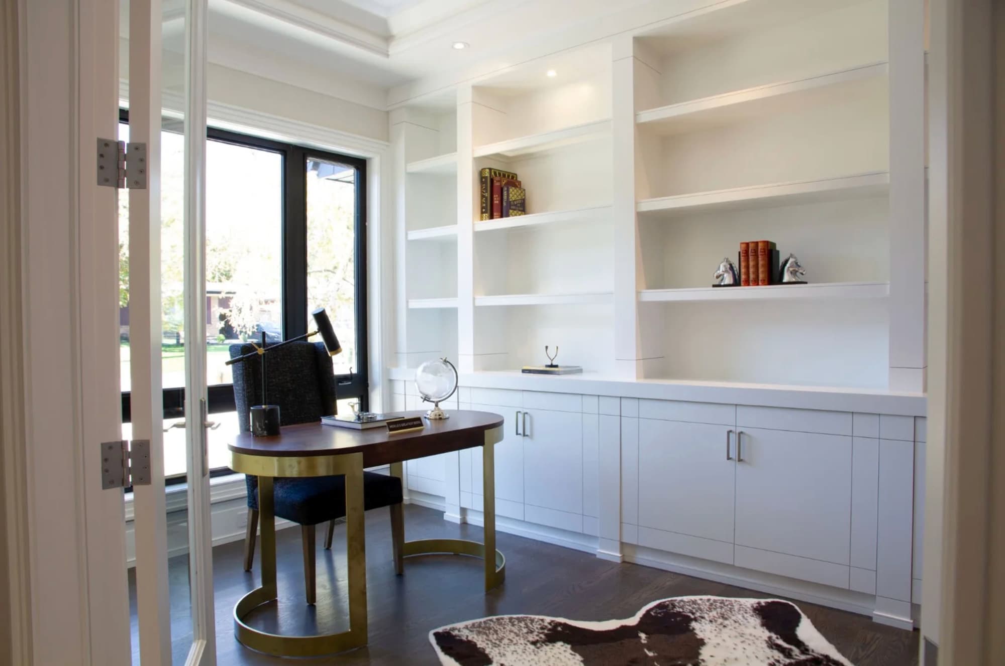 Home office with white built in shelving and cabinets beside a window