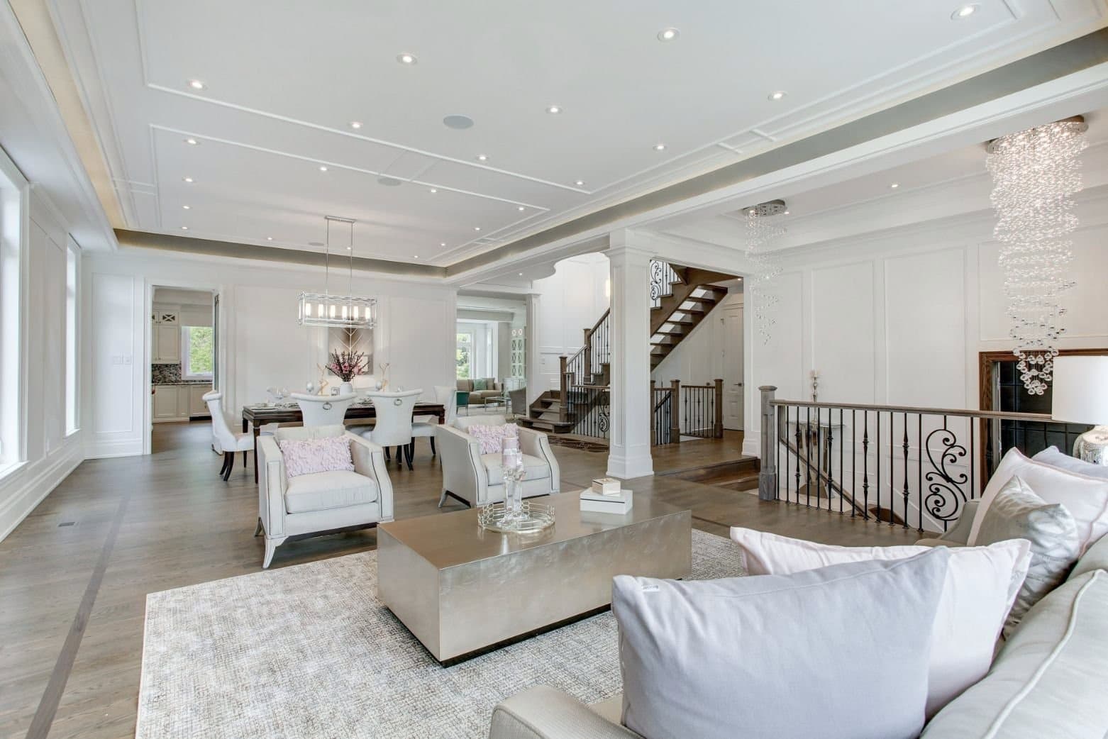 Open plan living and dining room with a tray ceiling, columns and wall panelling