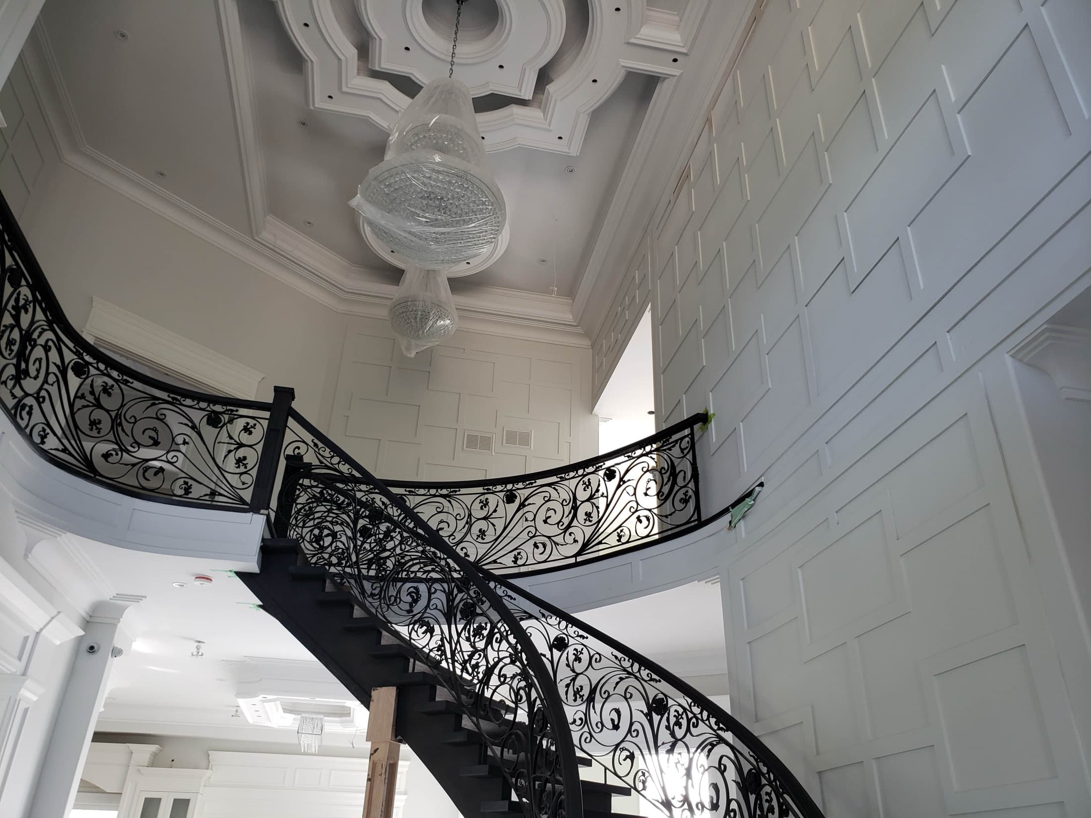 Curved staircase with an ornate wrought iron railing under a domed coffered ceiling