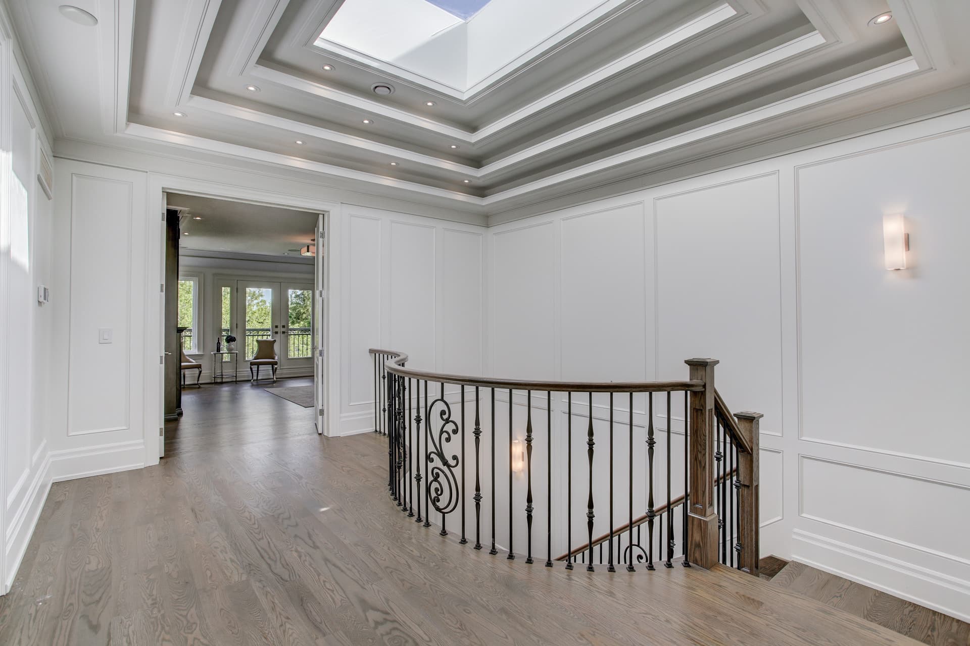 Upper hall with a tray ceiling skylight, wall panelling and a curved iron railing