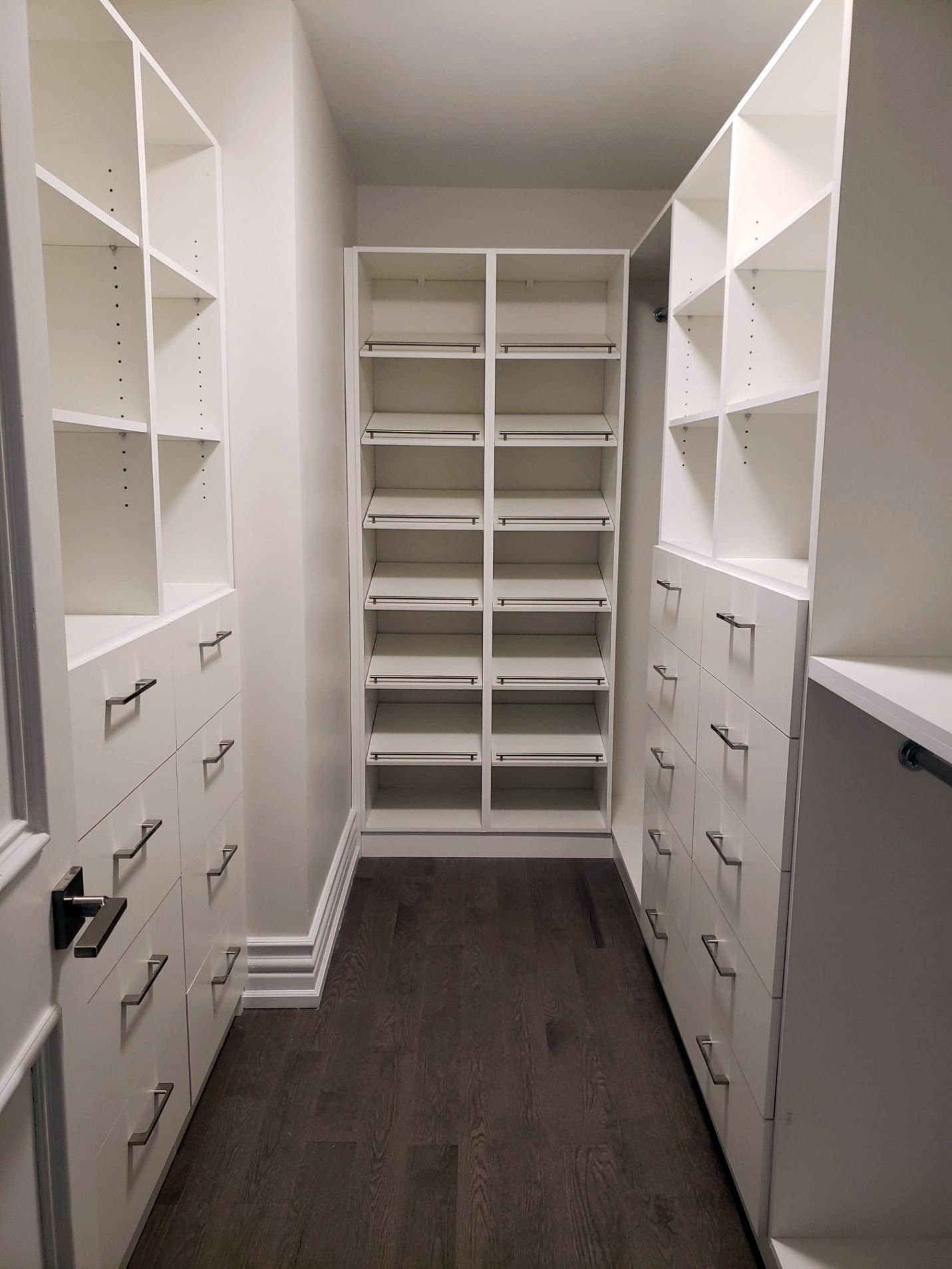 Walk in closet with floor to ceiling white shelving and banks of drawers