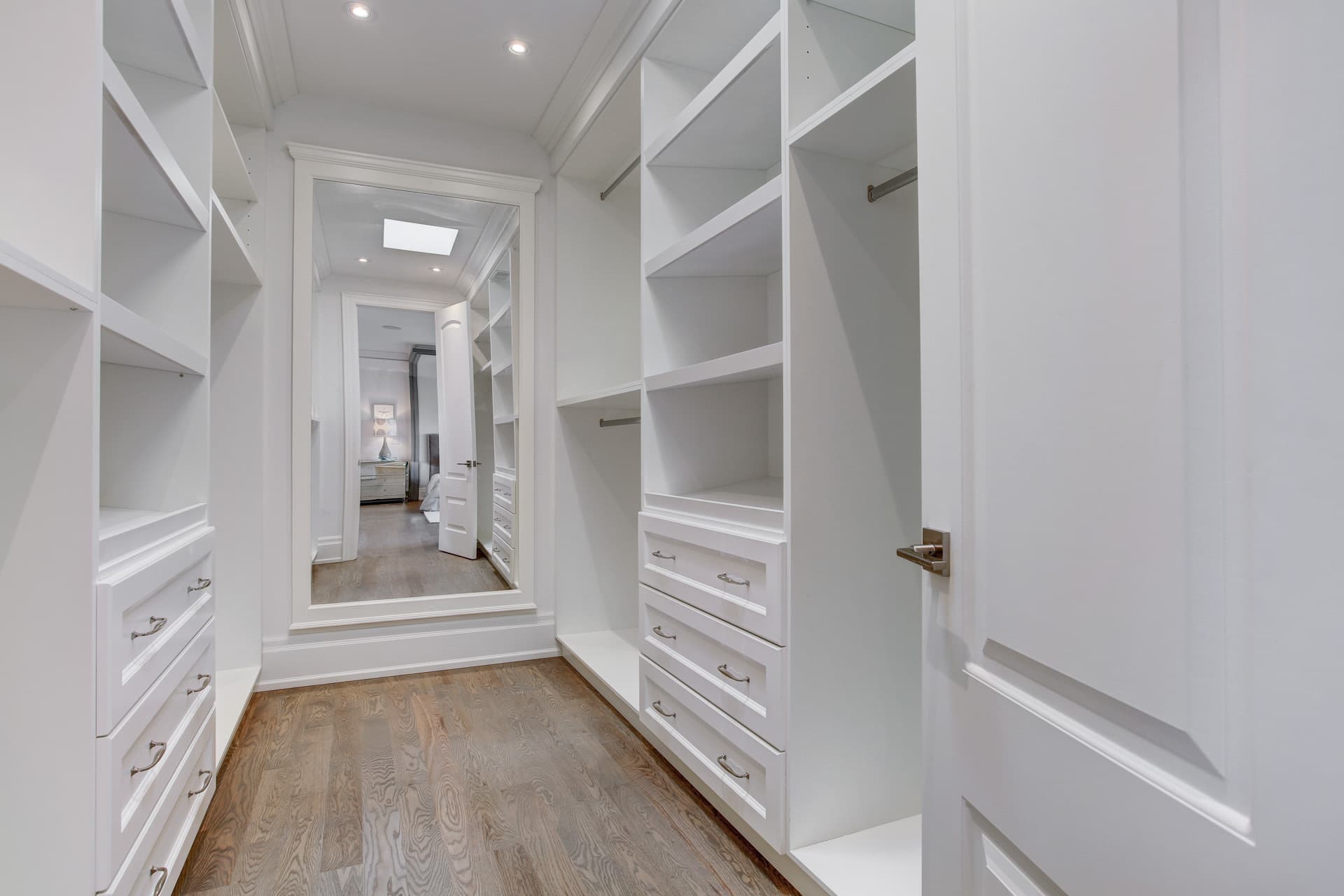 Walk in closet with white built in shelving, drawers and a full height mirror