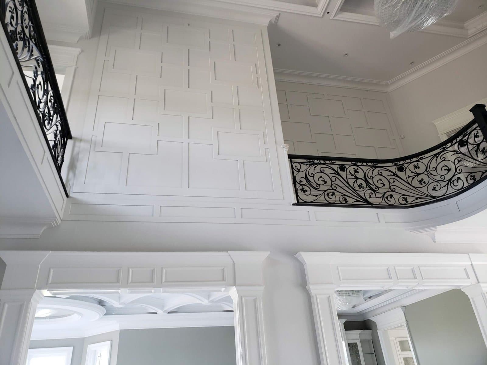 Two storey entrance hall with geometric wall panelling and an ornate iron railing